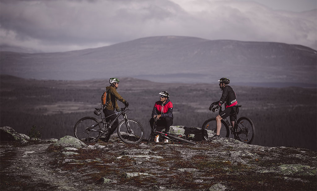 Tre män med cyklar pratar med varandra på en höjd i Funäsfjällen.